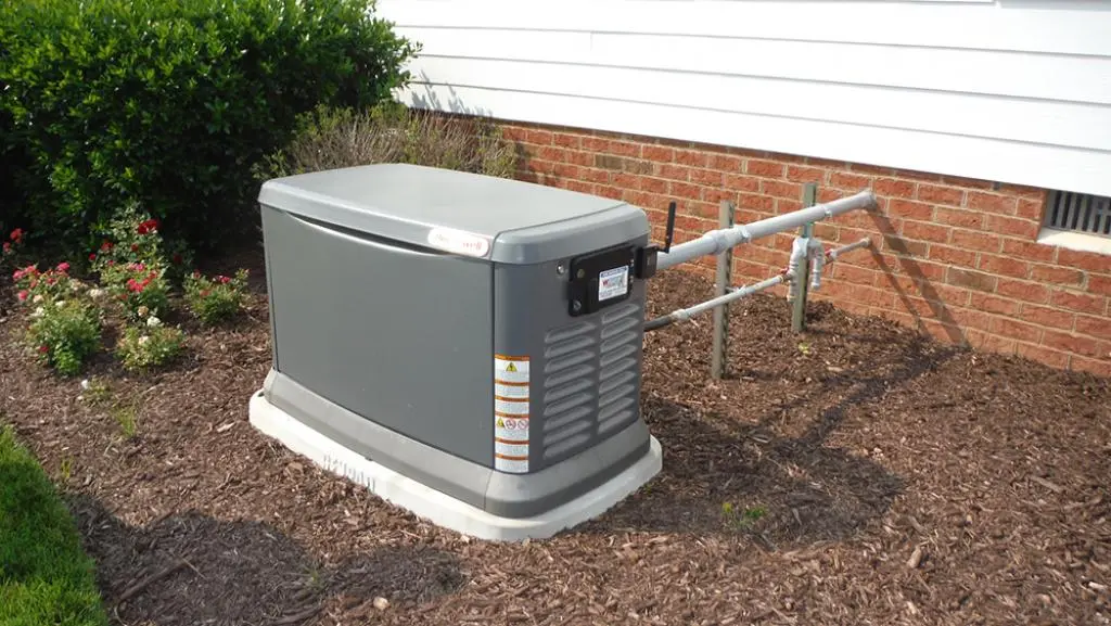 Whole house generators in mulch by brick house.